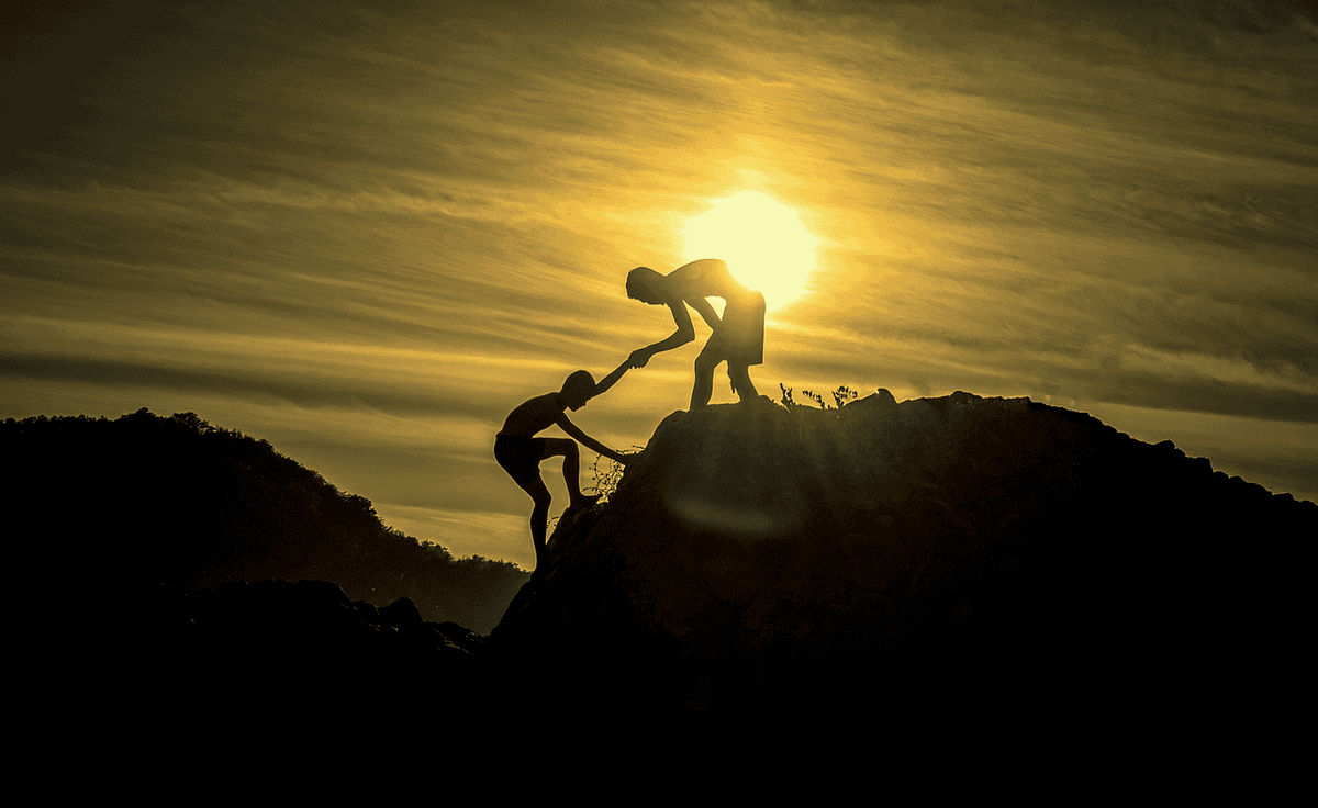 Two people supporting each other up a cliff. 