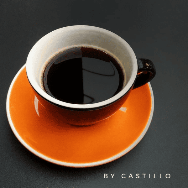 A picture of a orange cup with black coffee. By.Castillo logo on the bottom right corner.