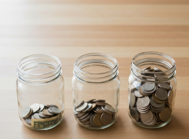Three clear glass jars on the table with different amounts of change. Illustration for the pay yourself first strategy.
